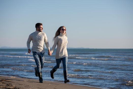 Young couple having fun walking and hugging on beach during autumn sunny day