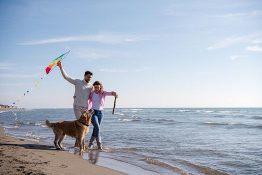 Young Couple having fun playing with a dog and Kite on the beach at autumn day