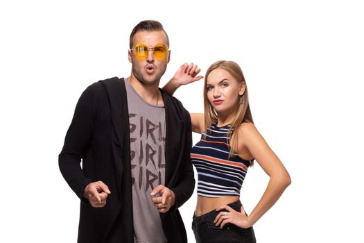 Hey you. Young adult man in yellow glasses, and cute blonde pointing fingers and looking at camera. On white background. Indoor, studio shot