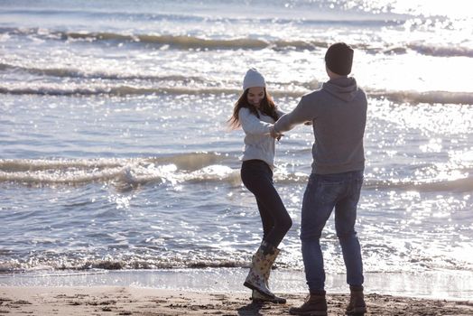 Young couple having fun walking and hugging on beach during autumn sunny day