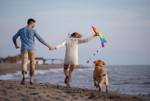 Young Couple having fun playing with a dog and Kite on the beach at autumn day