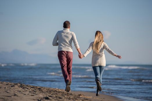 Young couple having fun walking and hugging on beach during autumn sunny day