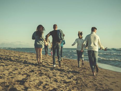 group of young friends spending day together running on the beach during autumn day colored filter