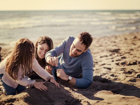 Family with little daughter resting and having fun at beach during autumn day colored filter