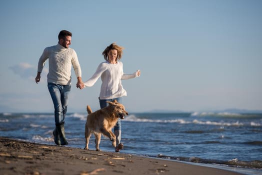 Couple Running On The Beach Holding Their Hands with dog On autmun day