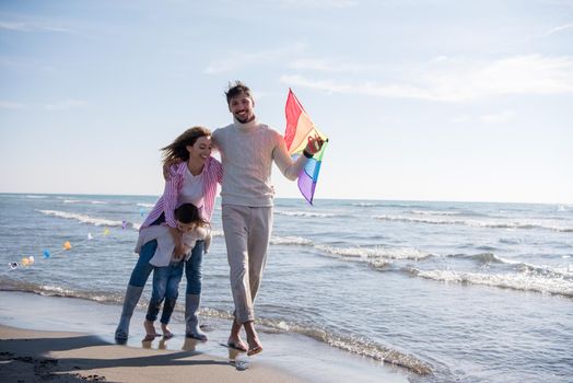 young family with kids resting and having fun with a kite at beach during autumn day