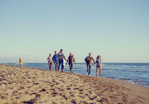 group of young friends spending day together running on the beach during autumn day colored filter