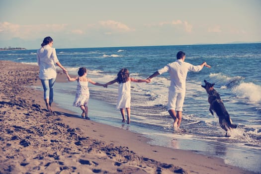 happy young family in white clothing have fun and play with beautiful dog at vacations on beautiful beach 