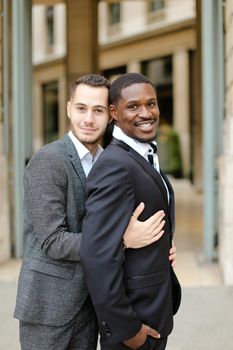 Caucasian man hugging afro american guy outside and wearing suit. Concept of happy same sex couple and gays.