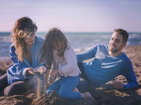 Family with little daughter resting and having fun at beach during autumn day colored filter