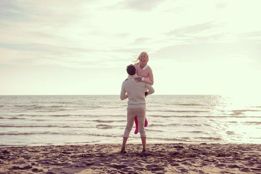 Young couple having fun walking and hugging on beach during autumn sunny day filter