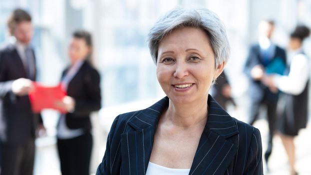 Happy successful mature Asian businesswoman posing in front of colleagues in business building