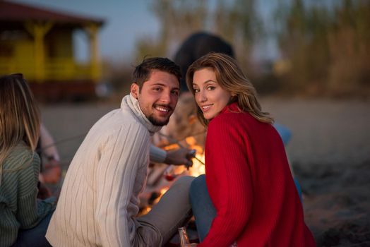 Young Couple enjoying with friends Around Campfire on The Beach At sunset drinking beer