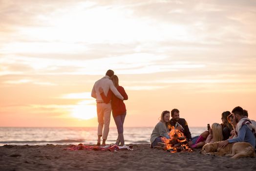 Young Couple enjoying with friends Around Campfire on The Beach At sunset drinking beer