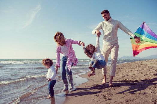 young family with kids resting and having fun with a kite at beach during autumn day filter