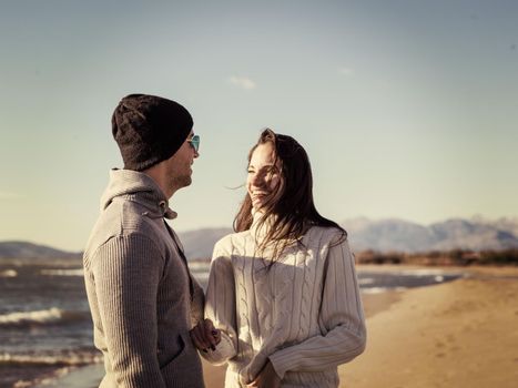 Young couple having fun walking and hugging on beach during autumn sunny day colored filter