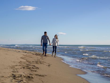 Young couple having fun walking and hugging on beach during autumn sunny day