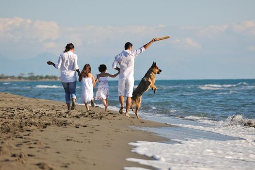 happy young family in white clothing have fun and play with beautiful dog at vacations on beautiful beach 