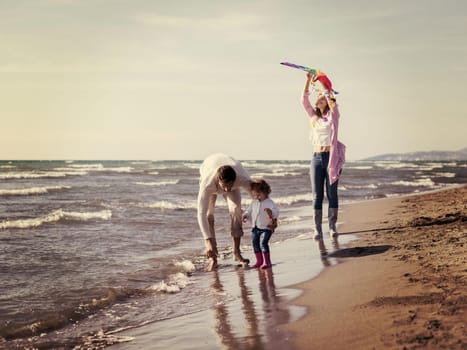 Family with little daughter resting and having fun with a kite at beach during autumn day colored filter