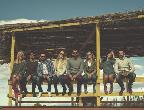 Happy Group Of Friends Hanging Out At Beach House having fun and drinking beer on autumn day colored filter