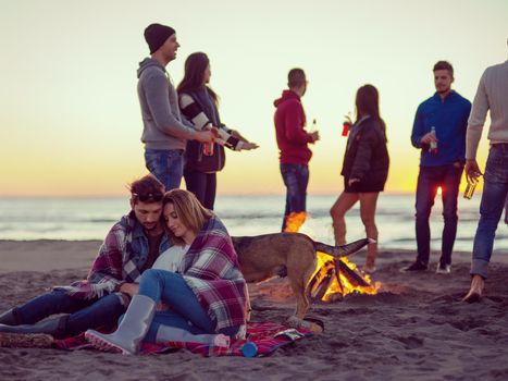 Young Couple Sitting with friends Around Campfire on The Beach At sunset drinking beer colored filter