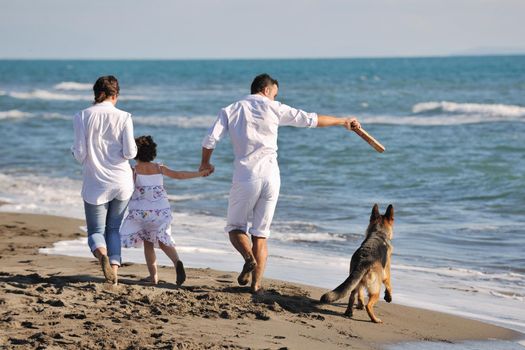 happy young family in white clothing have fun and play with beautiful dog at vacations on beautiful beach 