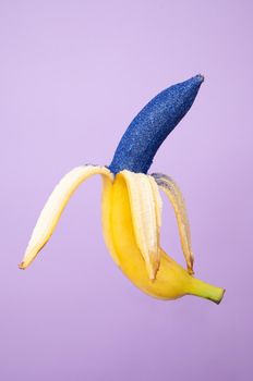 Peeled ripe banana covered with glittering paint of bright blue color and isolated on purple background