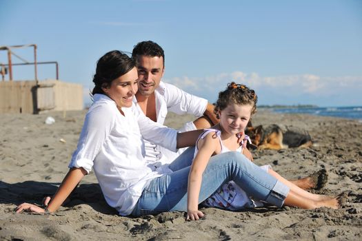 happy young family in white clothing have fun and play with beautiful dog at vacations on beautiful beach 