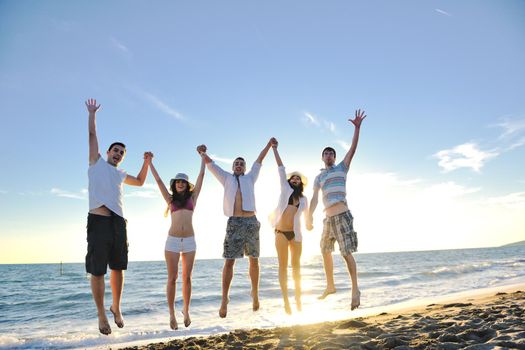 happy young friends group have fun and celebrate while jumping and running on the beach at the sunset