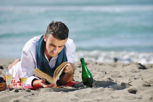 young man relaxing on beach at beautiful sunny day while reading book representing summer school and education concept