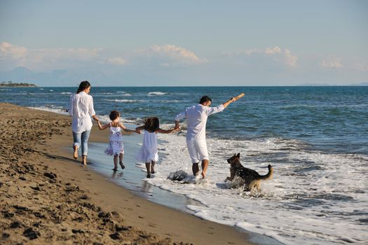 happy young family in white clothing have fun and play with beautiful dog at vacations on beautiful beach 