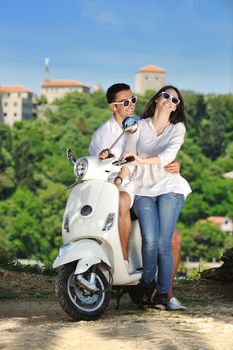 Portrait of happy young love couple on scooter enjoying themselves in a park at summer time