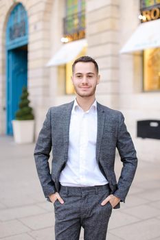 Young cacuasian male person wearing suit standing near building outdoors. Concept of fashion and businessman, urban life.