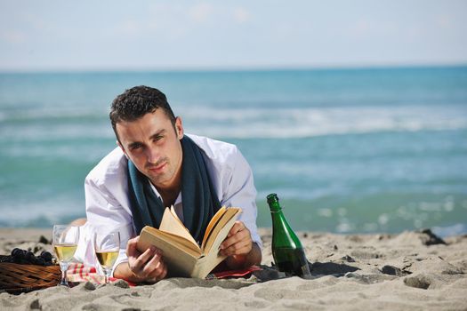 young man relaxing on beach at beautiful sunny day while reading book representing summer school and education concept