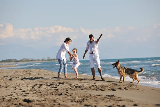 happy young family in white clothing have fun and play with beautiful dog at vacations on beautiful beach 