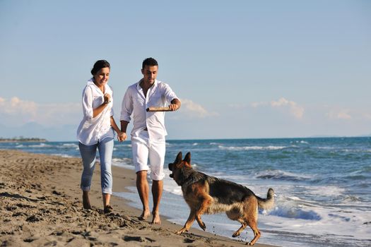 happy young family in white clothing have fun and play with beautiful dog at vacations on beautiful beach 