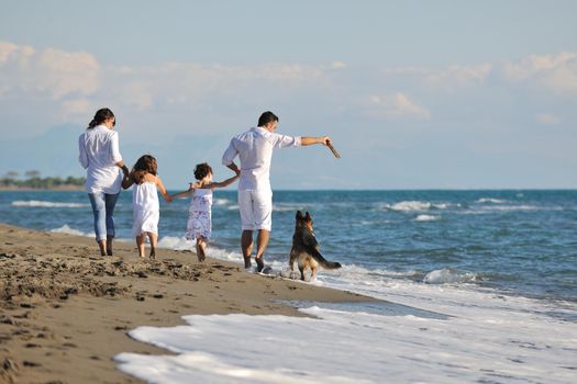 happy young family in white clothing have fun and play with beautiful dog at vacations on beautiful beach 