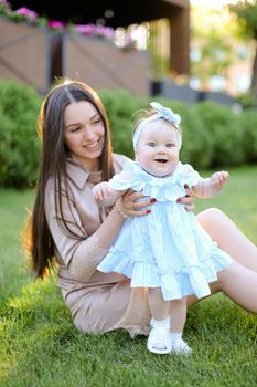 Young woman sitting on grass with little female baby. Concept of motherhood and children, resting on open air.