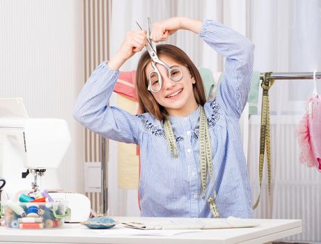 Cute young tailor with scissors at workspace