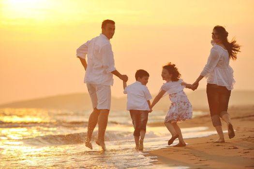 happy young family have fun on beach run and jump  at sunset