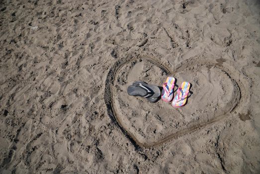 sandals in heart shape draving representing romance on beach concept