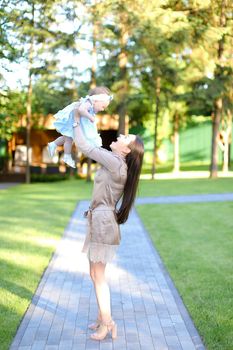 Young happy mother wearing dress holding little baby in garden. Concept of motherhood and resting on open air in park.