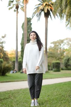 Asian nice woman walking in tropical park and wearing white sweater. Concept of nature and female person.