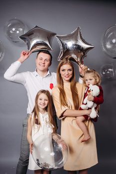 Joyous man and red-haired woman holding balloons and posing with two adorable children