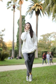 Asian beautiful woman walking in tropical park and wearing white sweater. Concept of nature and female person.