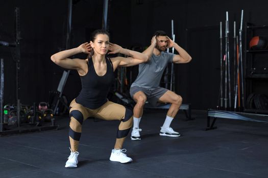 Fitness couple in sportswear doing squat exercises at gym