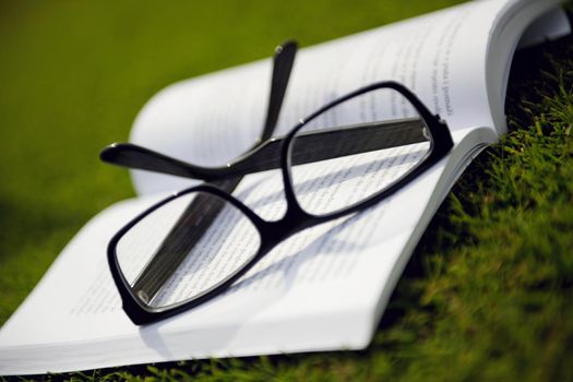 Glasses on a book outside with grass inbbacground, education relax and study concept