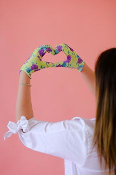 Woman wearing gloves and showing heart gesture by hands in pink monophonic background with copyspace. Concept of love and positive.