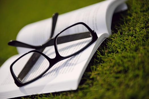 Glasses on a book outside with grass inbbacground, education relax and study concept