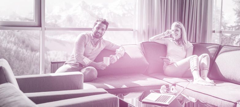 Young couple relaxing at  home using tablet computer reading in the living room near the window on the sofa couch.